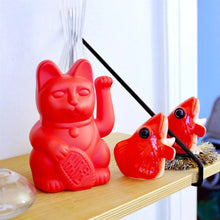 Charger l'image dans la galerie, Figurine Maneki Neko Lucky Cat rouge placée sur une étagère en bois clair, à côté d'autres objets décoratifs rouges