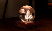 Load image into Gallery viewer, Veilleuse boule de cristal 3D de Gingko Design avec motif de chouette sous la lune posée sur son socle en bois de noyer illuminé.